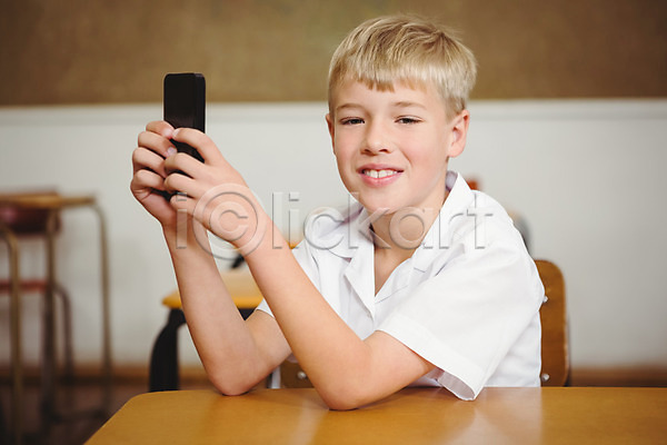 행복 남자 백인 소년 어린이 한명 JPG 포토 해외이미지 교실 교육 미소(표정) 수업 스마트폰 신학기 실내 앉기 잡기 책상 초등학교 학교 학생 학습 해외202004 핸드폰