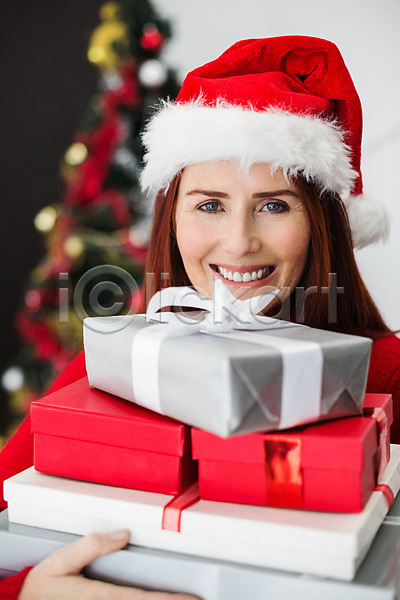축하 행복 40대 백인 여자 중년 한명 JPG 포토 해외이미지 가정 거실 라이프스타일 미소(표정) 빨간머리 산타모자 선물 실내 쌓기 장식 장식볼 축제 크리스마스 크리스마스장식 크리스마스트리 해외202004