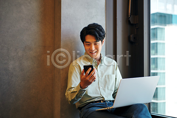 20대 남자 성인 성인남자한명만 한국인 한명 JPG 앞모습 포토 노트북 들기 라운지 미소(표정) 비즈니스 비즈니스맨 사무실 상반신 스마트폰 실내 앉기 업무 응시 직장 창업 회사