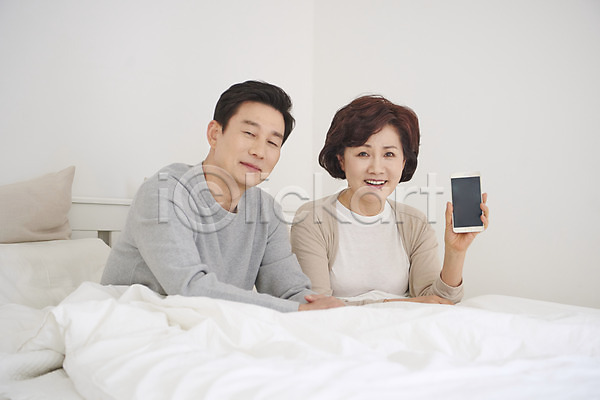 즐거움 50대 남자 두명 여자 중년 중년만 한국인 JPG 앞모습 포토 갱년기 들기 미소(표정) 보여주기 부부 상반신 스마트폰 실내 앉기 중년부부 침대 침실 흰색