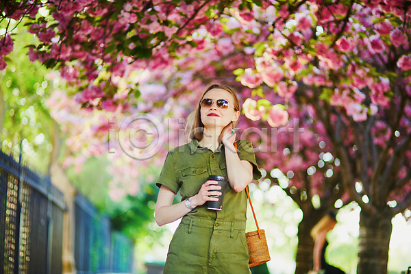 백인 성인 성인여자한명만 여자 외국인 한명 JPG 아웃포커스 앞모습 포토 해외이미지 가방 공원 나무 들기 벚꽃 봄 상반신 야외 주간 테이크아웃컵 파리(프랑스)
