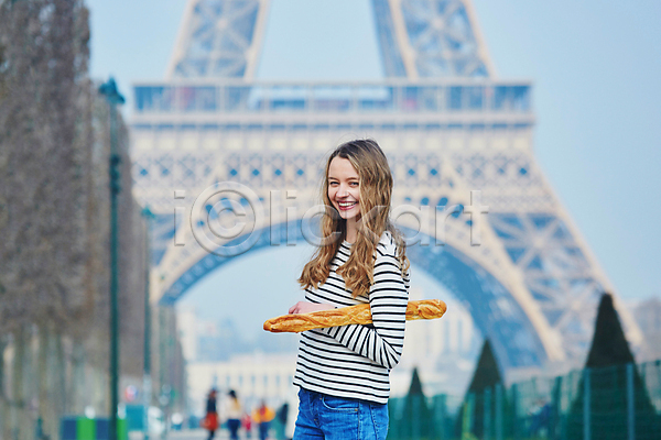 백인 성인 성인여자한명만 여자 한명 JPG 아웃포커스 옆모습 포토 해외이미지 거리 들기 미소(표정) 바게트 상반신 야외 에펠탑 주간 파리(프랑스)