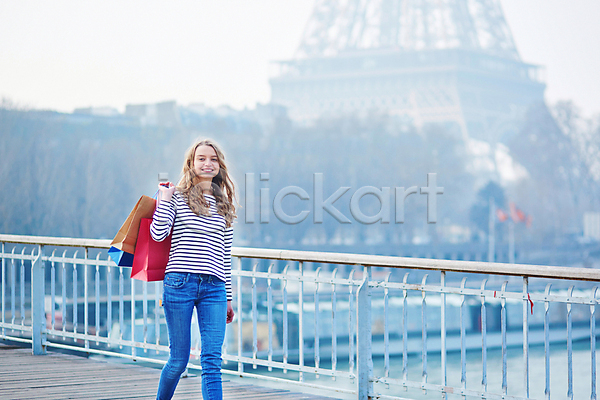 백인 성인 성인여자한명만 여자 한명 JPG 아웃포커스 앞모습 포토 해외이미지 거리 들기 미소(표정) 상반신 쇼핑백 야외 에펠탑 주간 파리(프랑스)