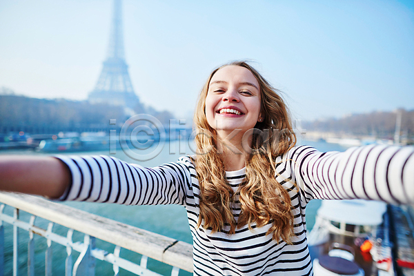 백인 성인 성인여자한명만 여자 한명 JPG 아웃포커스 앞모습 포토 해외이미지 거리 미소(표정) 상반신 셀프카메라 야외 에펠탑 주간 파리(프랑스) 팔벌리기