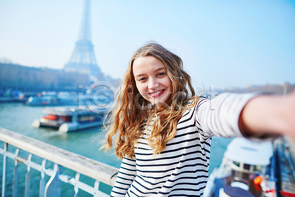 백인 성인 성인여자한명만 여자 한명 JPG 아웃포커스 앞모습 포토 해외이미지 거리 미소(표정) 상반신 셀프카메라 손들기 야외 에펠탑 주간 파리(프랑스)