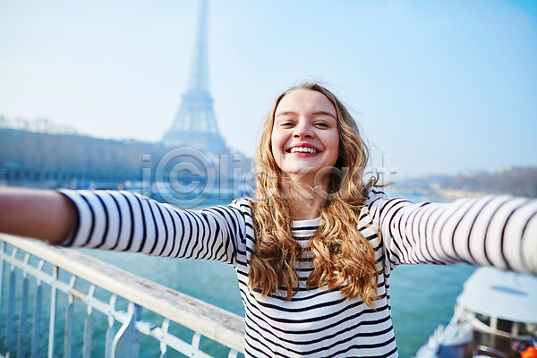 백인 성인 성인여자한명만 여자 한명 JPG 아웃포커스 앞모습 포토 해외이미지 거리 미소(표정) 상반신 셀프카메라 손들기 야외 에펠탑 주간 파리(프랑스)