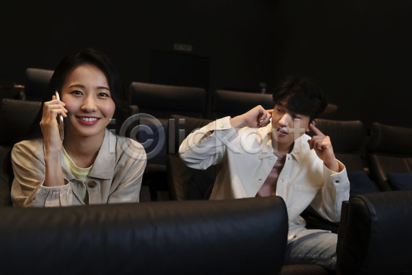 20대 남자 두명 성인 성인만 여자 한국인 JPG 앞모습 포토 공공장소 귀막기 들기 미소(표정) 비매너 상반신 스마트폰 실내 앉기 어둠 영화관 영화관람 응시 통화