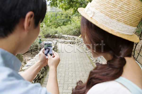 20대 남자 동양인 두명 사람 성인 성인만 여자 청년만 한국인 JPG 뒷모습 포토 동물원 들기 모자(잡화) 사진촬영 상반신 스마트폰 야외 주간 커플 핸드폰