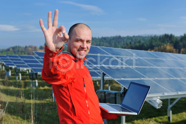 남자 성인 성인남자한명만 한명 JPG 옆모습 포토 해외이미지 OK 노트북 들기 미소(표정) 상반신 야외 주간 집열판 태양에너지 하늘 해외202004
